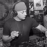 A black and white photo of a DJ wearing a backwards baseball cap and headphones