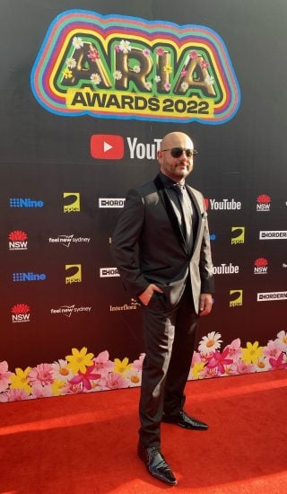 IMG_4474 A man in a black suit and sunglasses poses on a red carpet in front of an "ARIA AWARDS 2022" backdrop featuring various sponsor logos.